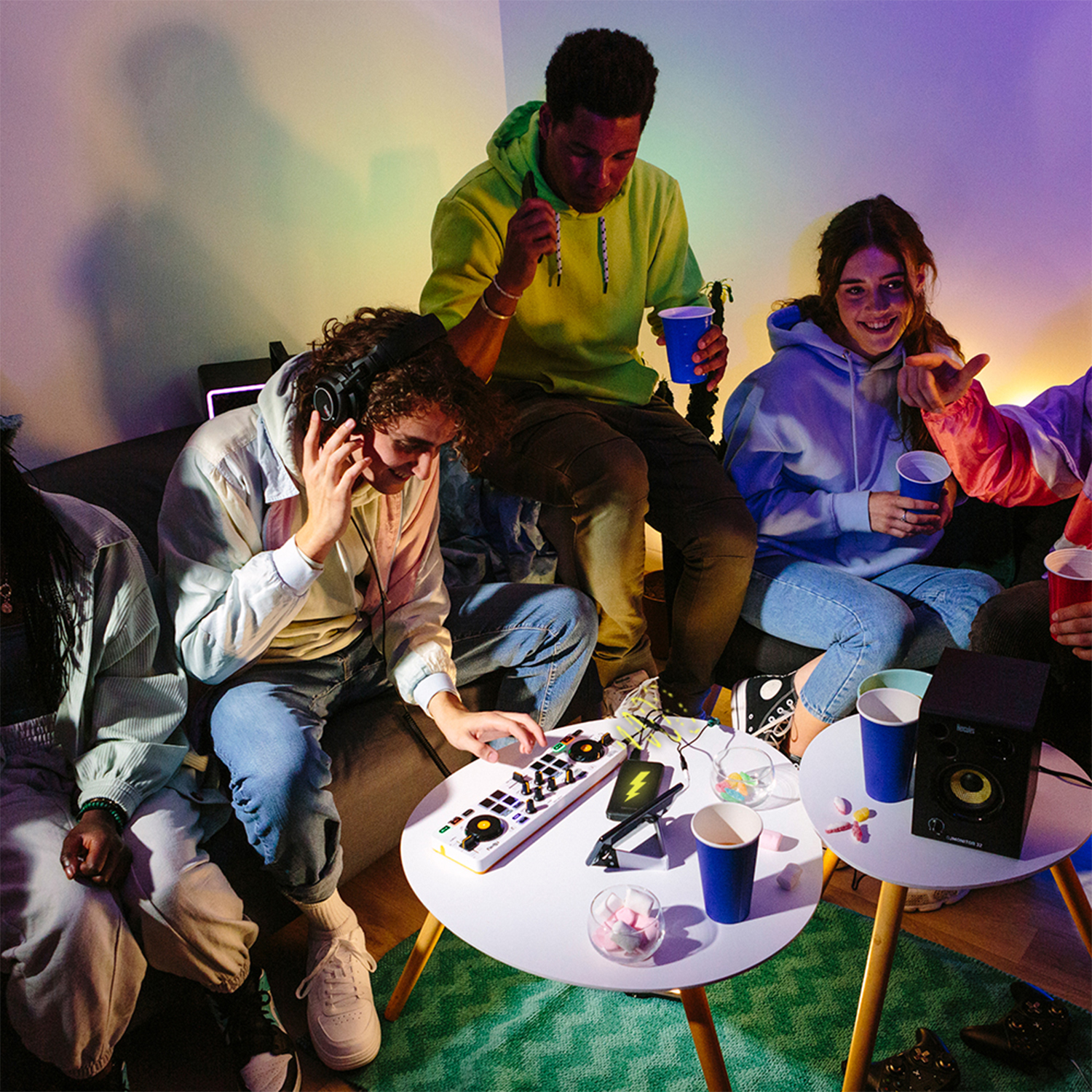 Gruppo di persone a una festa. Sono seduti attorno a un tavolo con bevande e un'attrezzatura da DJ.