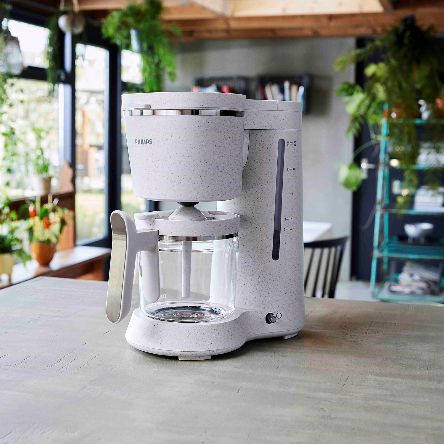 Caffettiera Philips bianca con caraffa in vetro su un piano di lavoro tipo cemento, con sfondo.