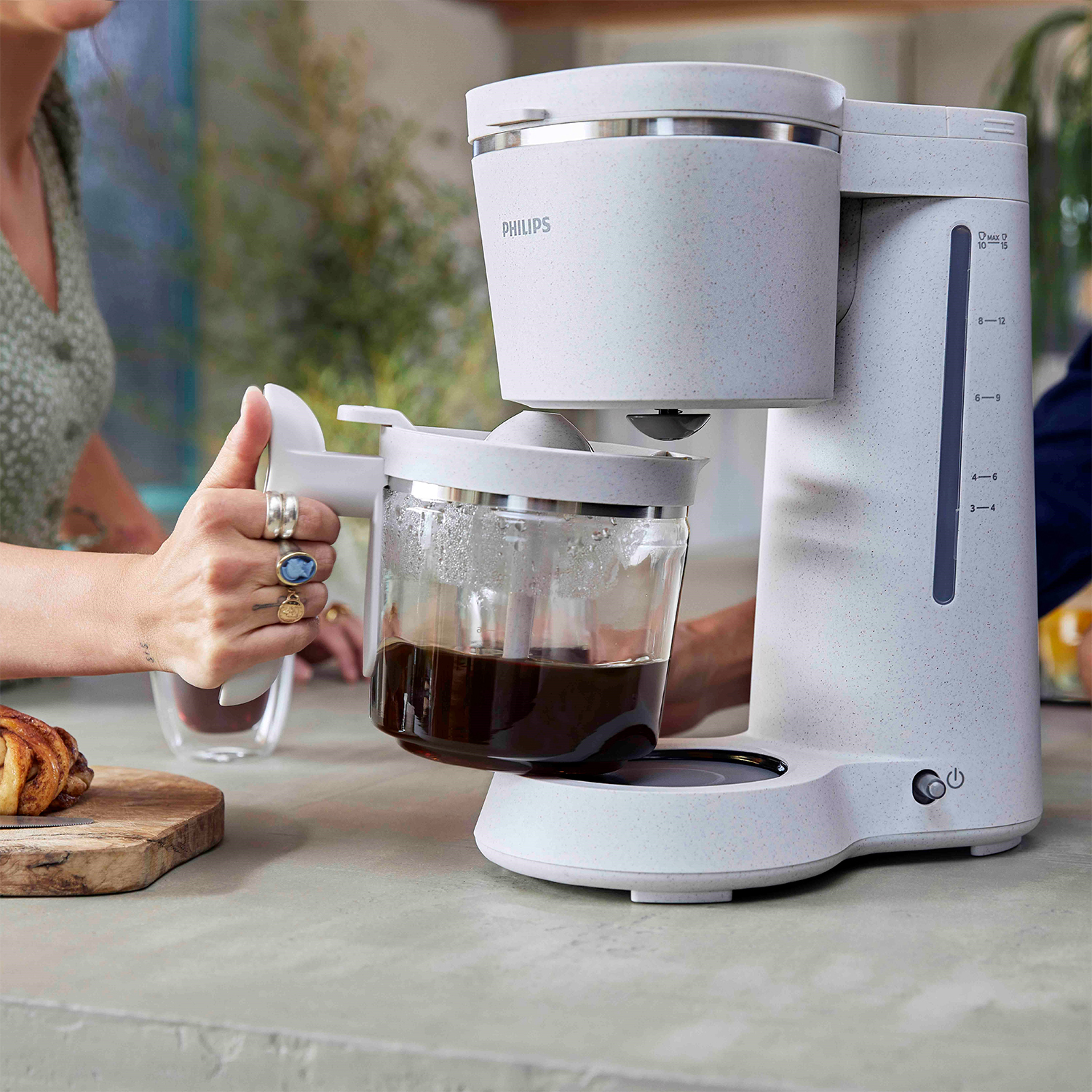 Macchina da caffè con caraffa in vetro, una mano la tiene e un piano di lavoro.