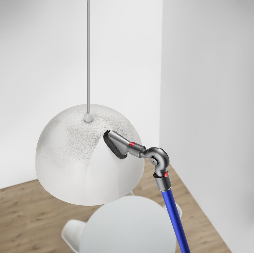 Bir elektrikli süpürge, fırça aparatı ile beyaz bir lambayı temizliyor.