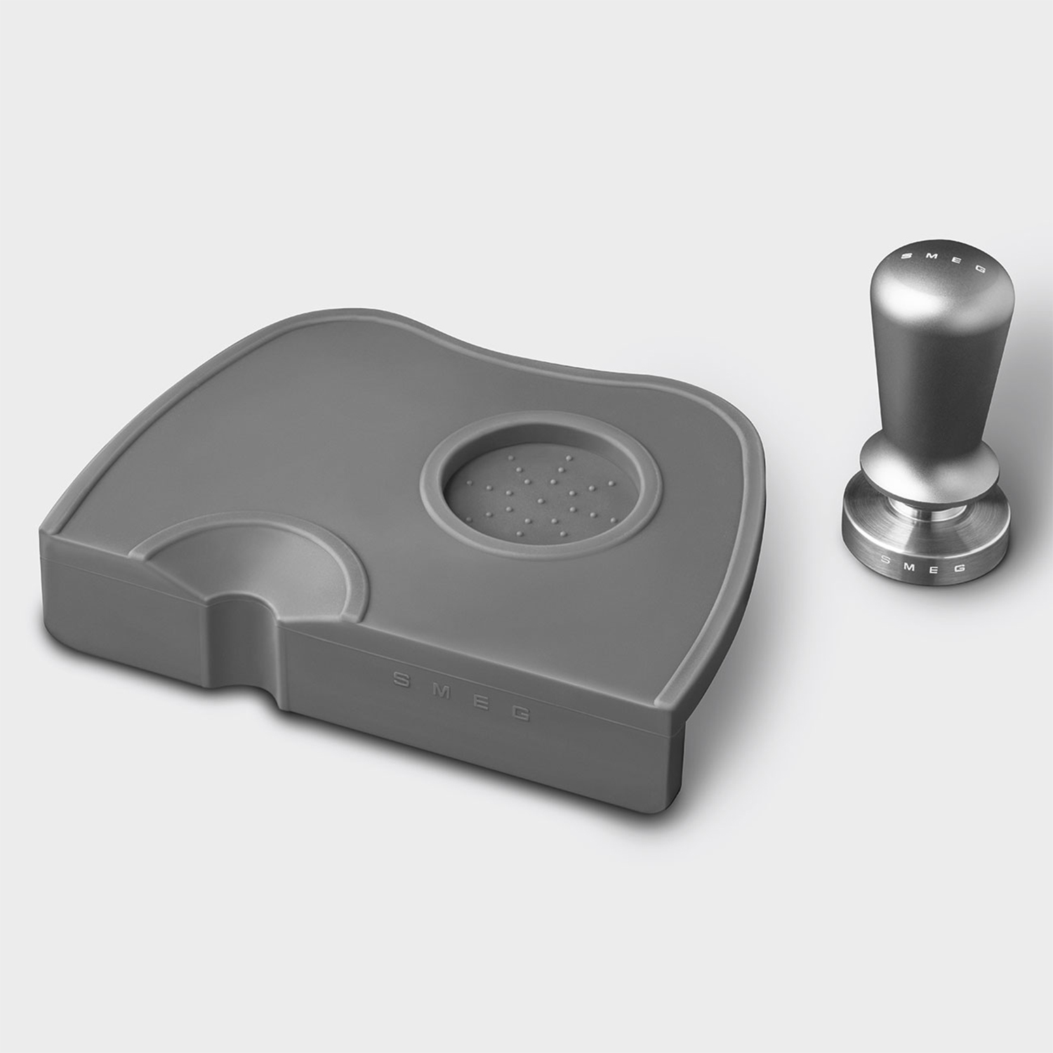Pressino per caffè grigio e tappetino grigio. SMEG è etichettato sul tappetino.