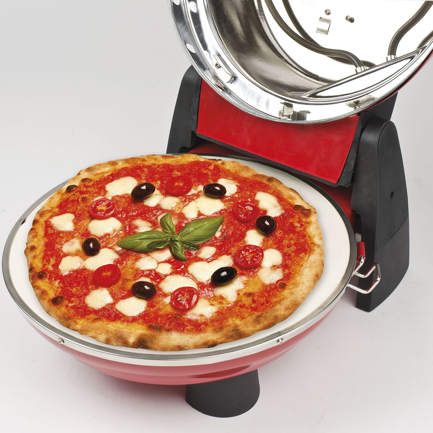Una pizza su un piatto bianco all'interno di un forno per pizza rosso. La pizza ha pomodori, olive e basilico.