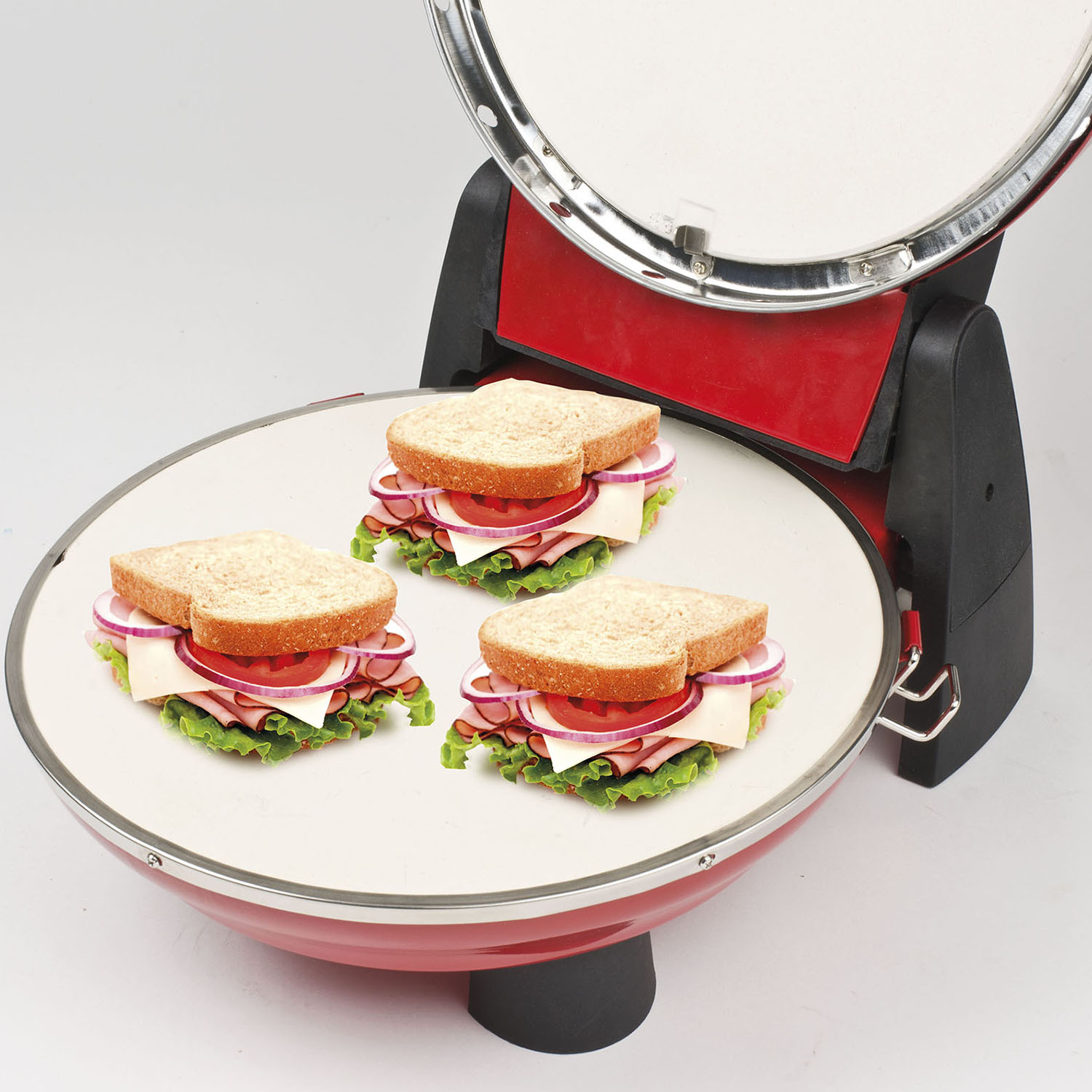 Tre panini su una griglia rossa e argento. Ognuno ha pane, lattuga, pomodoro e formaggio.