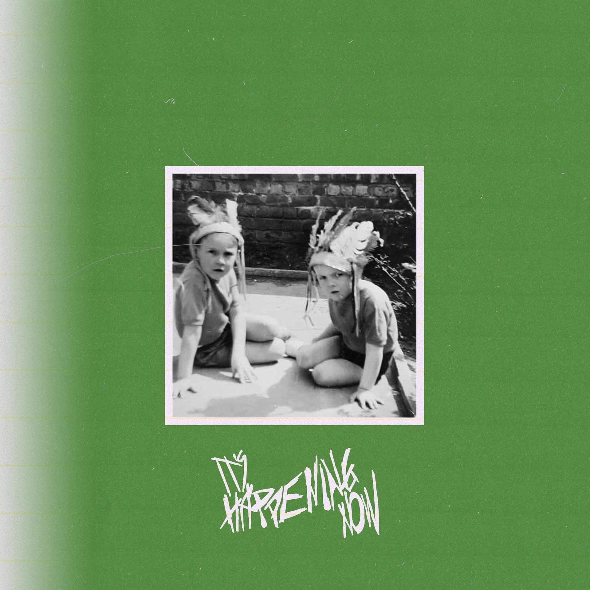 Pochette de l'album : The Happening Now. Deux enfants portant des coiffes à plumes sur fond vert.