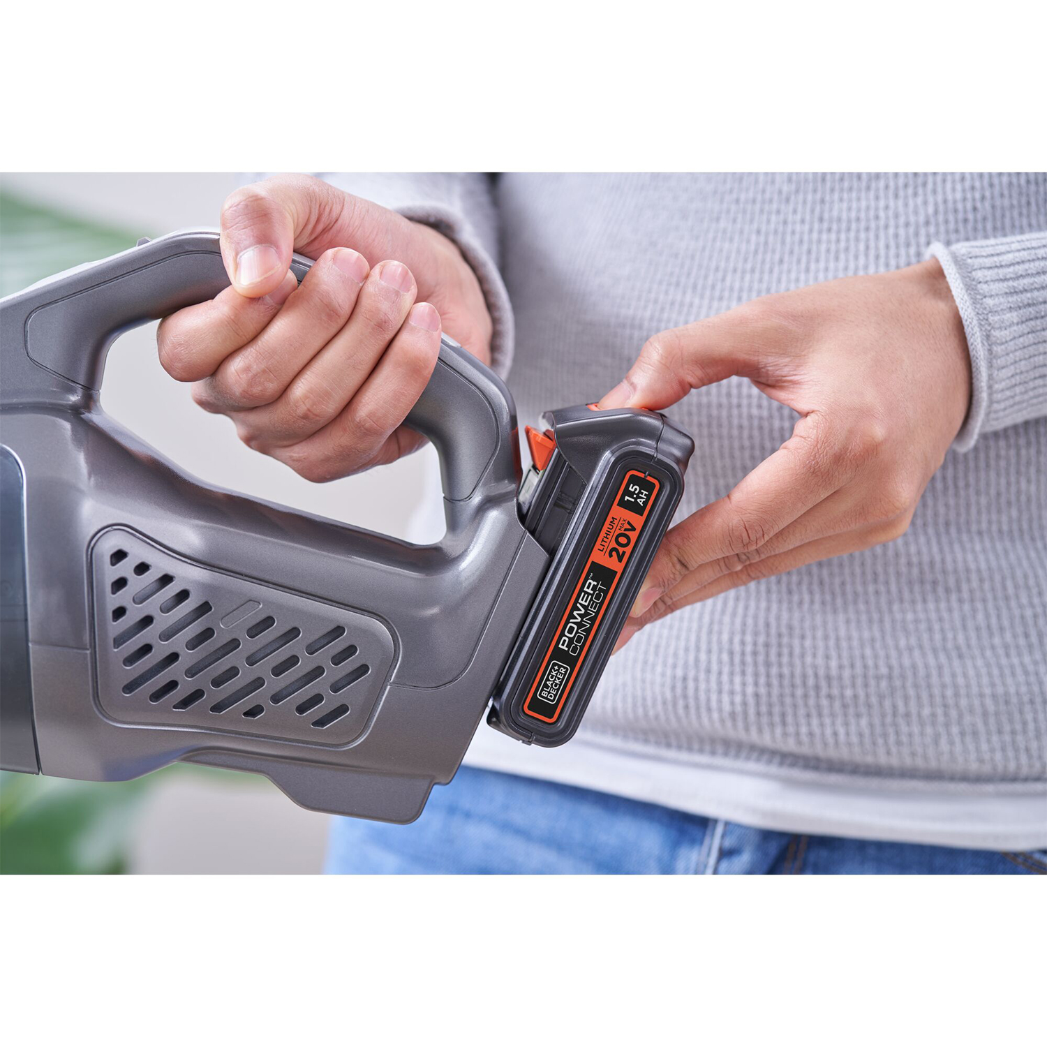 Mani di una persona che inserisce una batteria in un aspirapolvere grigio Black+Decker.