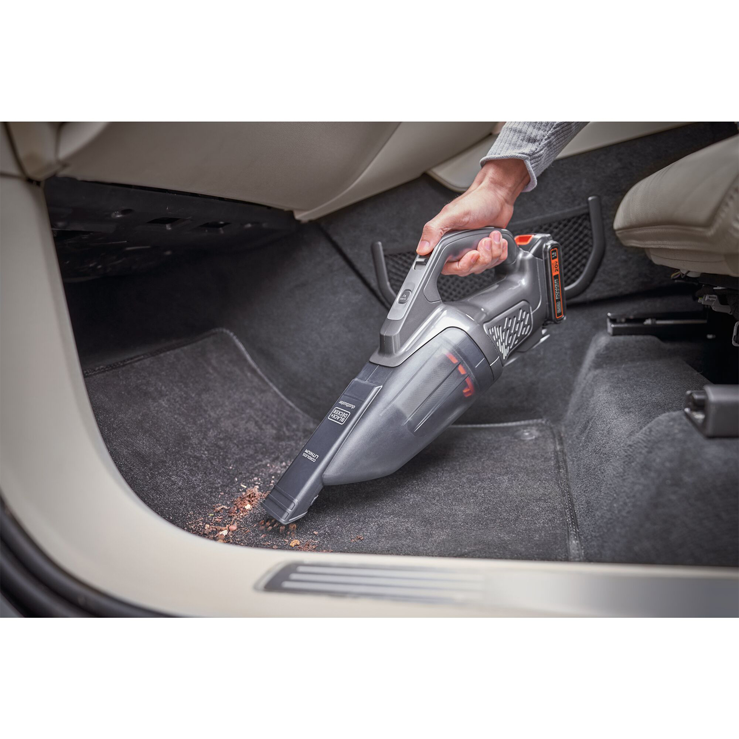 Una persona usa un aspirapolvere portatile all'interno di un'auto per pulire la moquette.