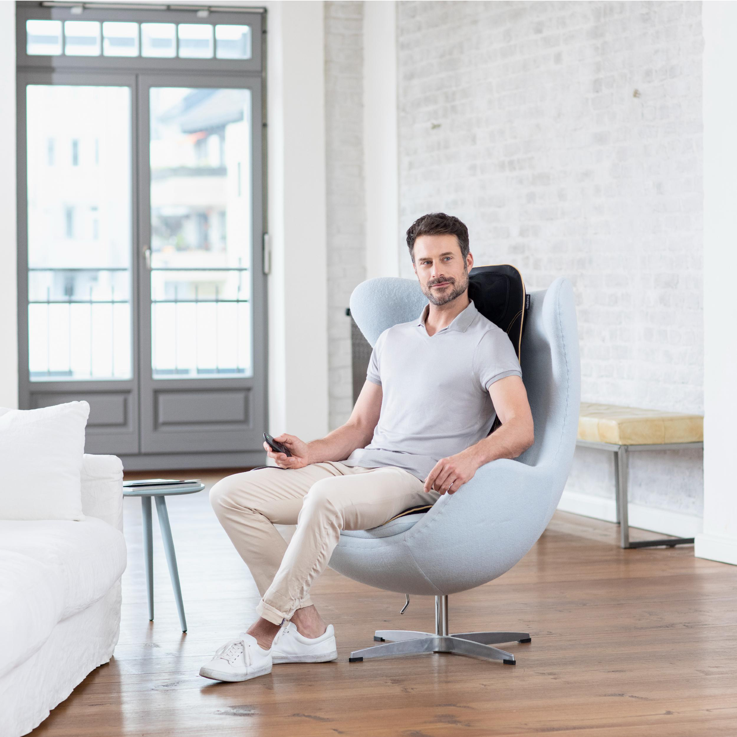 Ein Mann in grauem Hemd entspannt sich in einem blauen Stuhl mit einem Massagegerät.