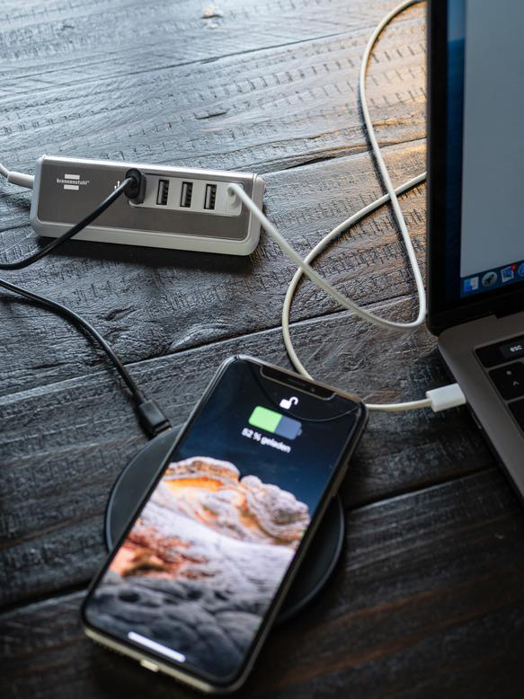 Ein Smartphone, das auf einem kabellosen Ladegerät neben einem Laptop und Hub geladen wird.
