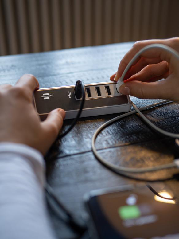 Hände stecken Kabel in einen USB-Hub auf einem Holztisch.