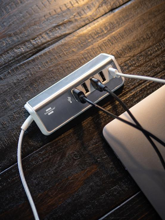 USB-Hub mit mehreren angeschlossenen Kabeln auf Holzoberfläche.