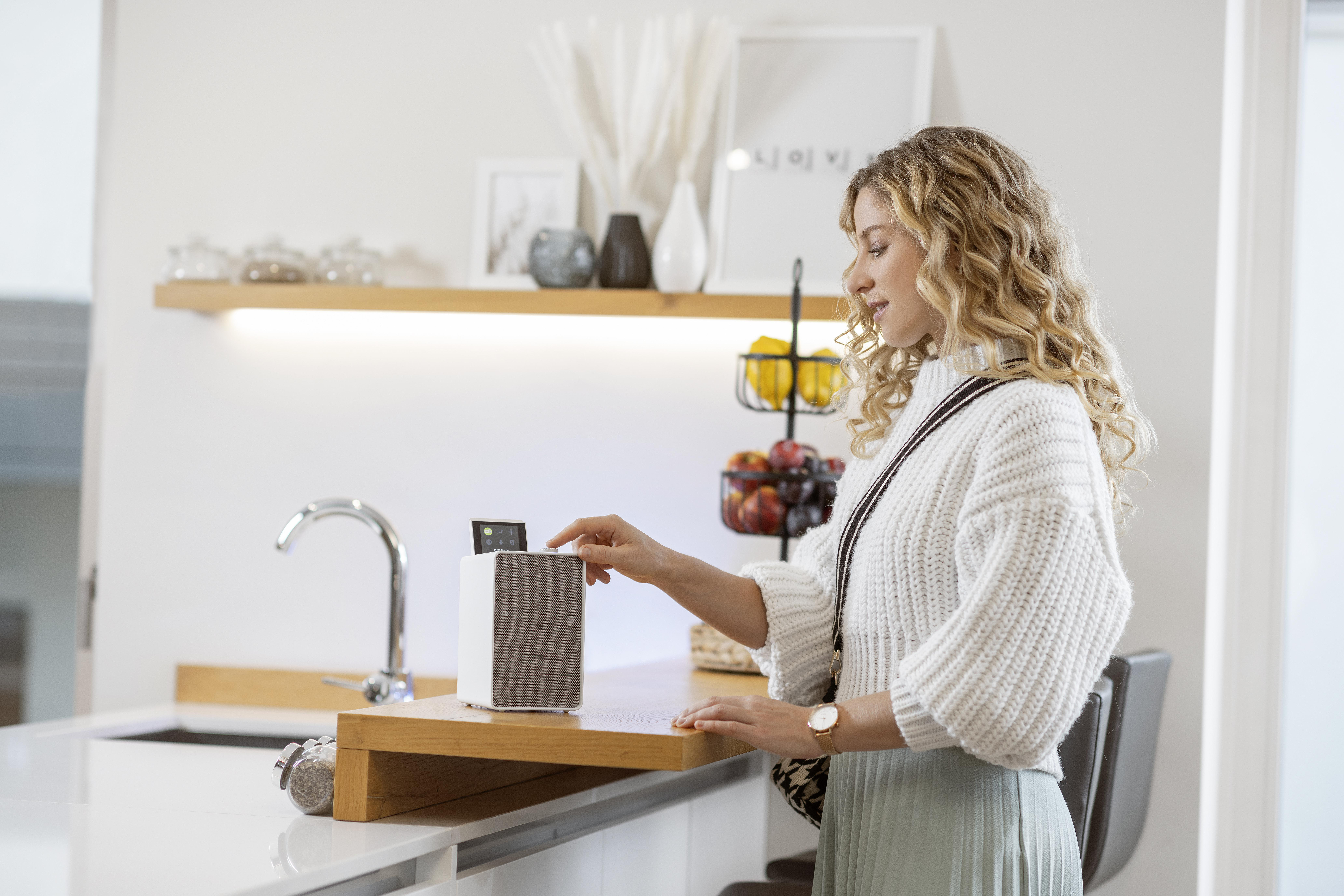 Frau in der Küche benutzt einen Lautsprecher auf einem Holzständer. Küchenhintergrund.