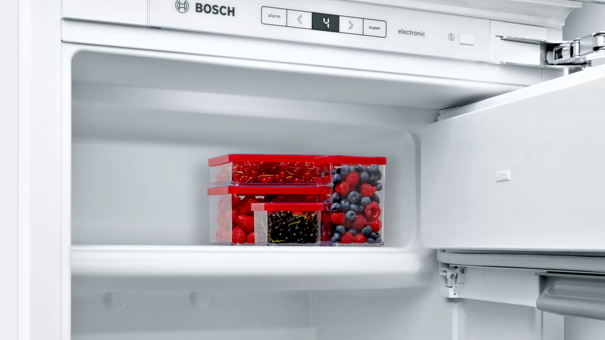 In einem weißen Kühlschrank mit Regalen und Behältern, die mit Beeren gefüllt sind. Die Tür ist geöffnet.