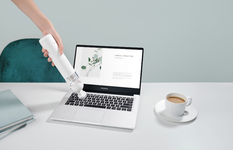 Egy személy egy kézi porszívóval tisztítja a laptop billentyűzetét.