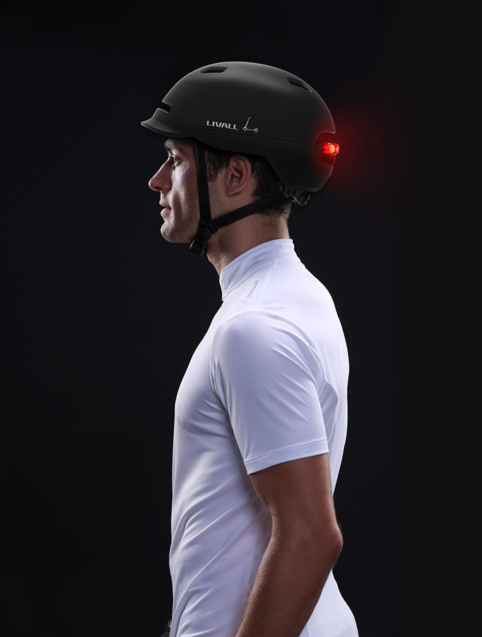 Uomo in camicia bianca con casco nero con luce rossa. Vista di profilo su sfondo nero.
