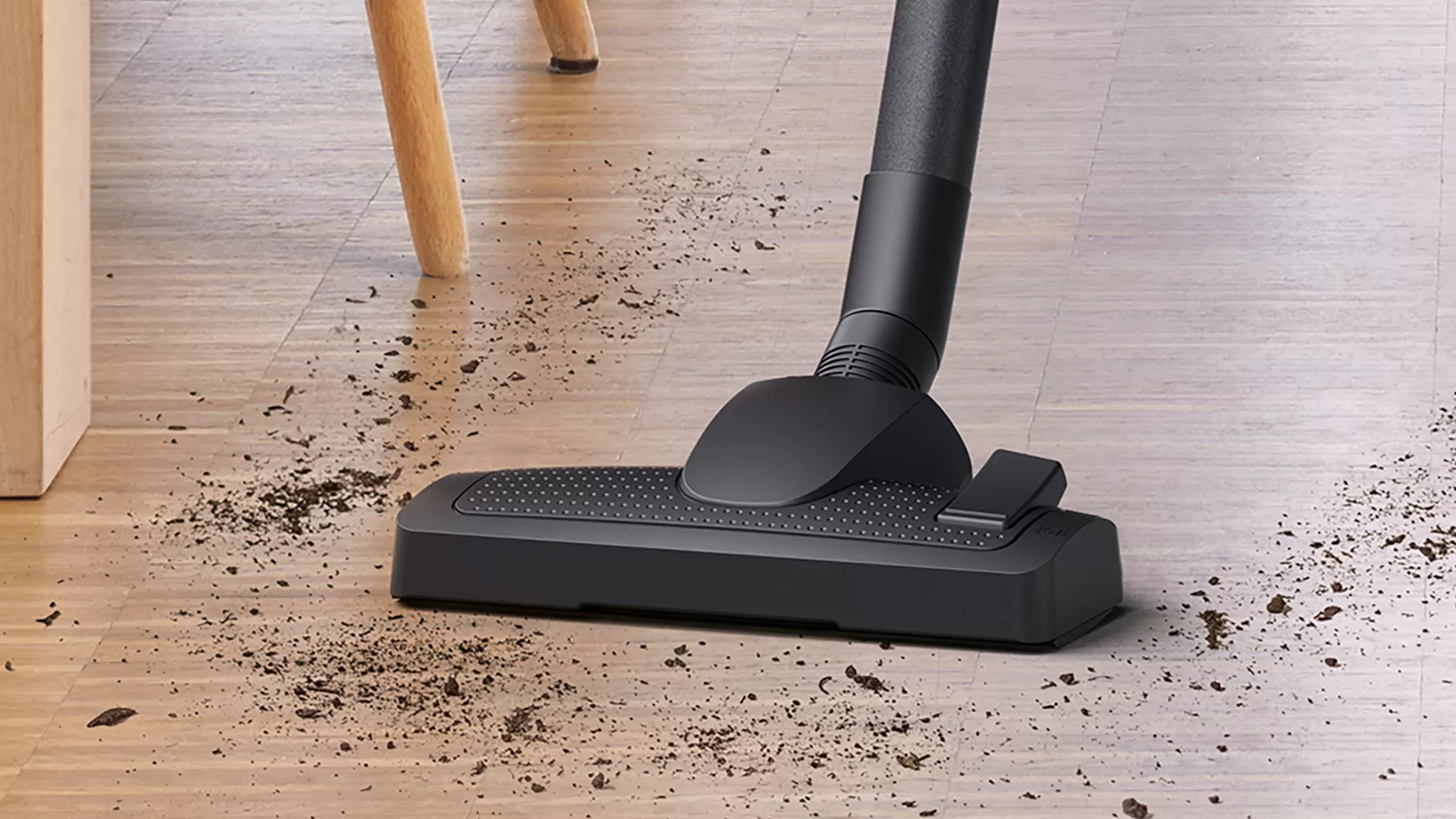 Vacuum cleaner head with scattered dirt on a wood floor. Wooden leg is seen.