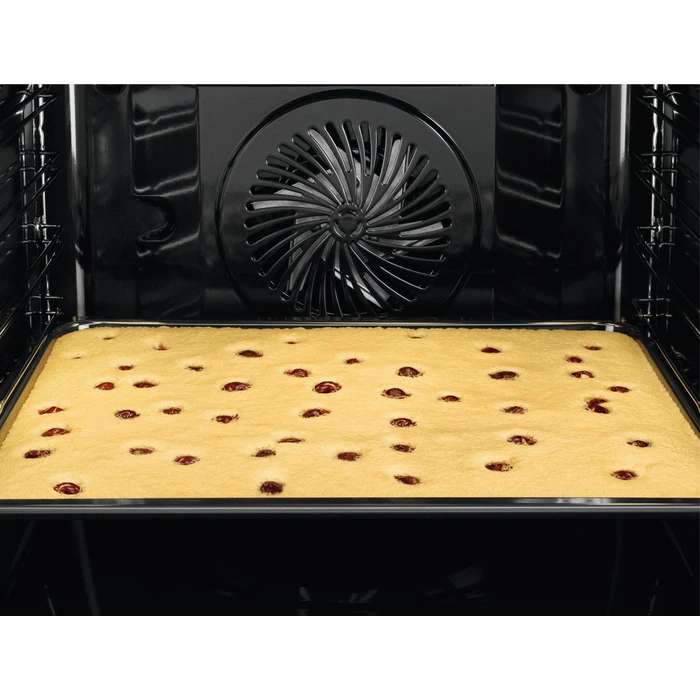 In een zwarte oven met een gebakken cake. De cake is geel met rode stippen, met een ventilator achterin.