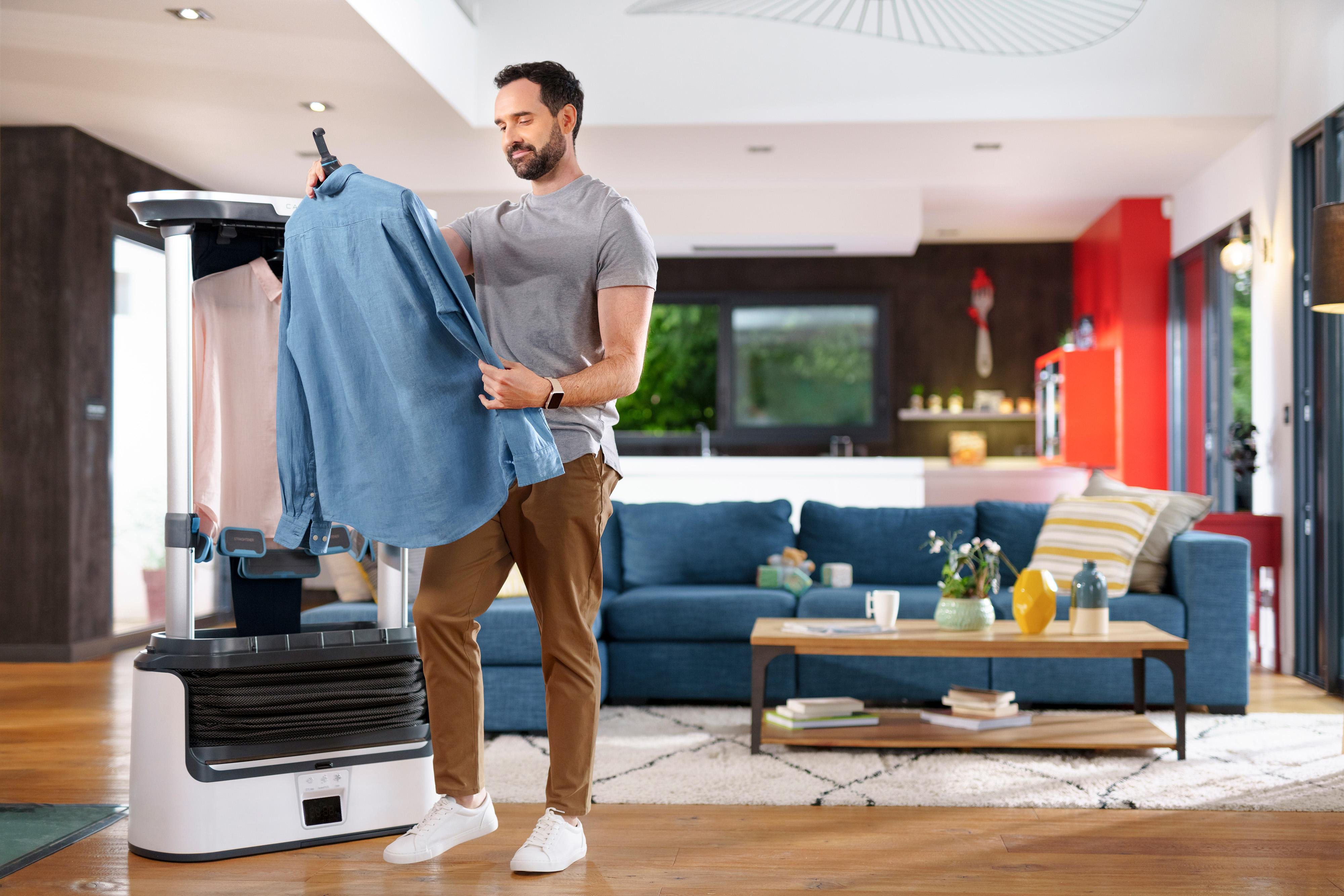 Mann in einem Raum, der ein Hemd auf ein Roboter-Kleidungspflegesystem legt.