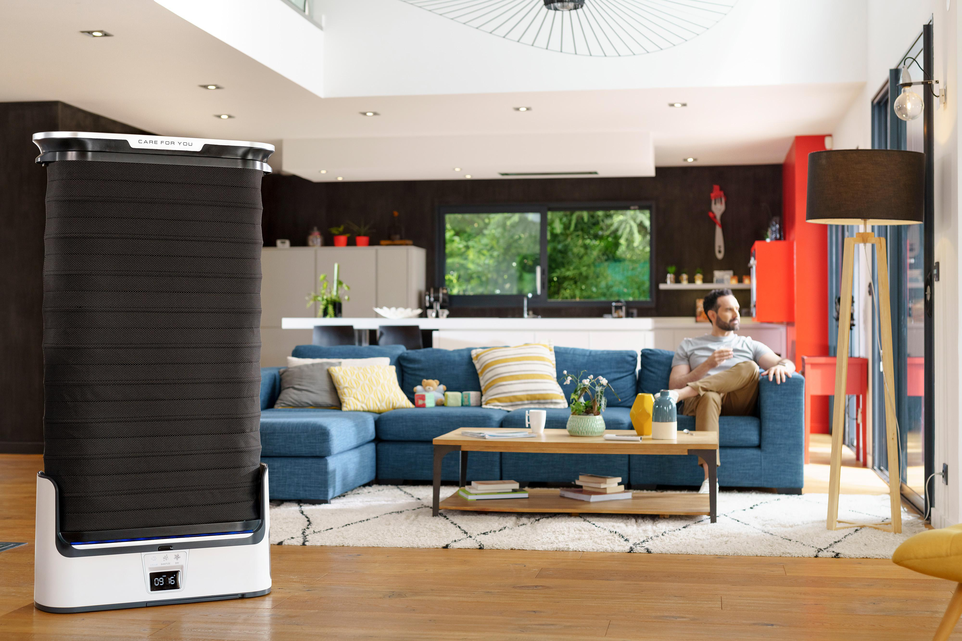 Wohnzimmer mit Roboter. Blaues Sofa, Couchtisch, Mann sitzt auf dem Sofa.