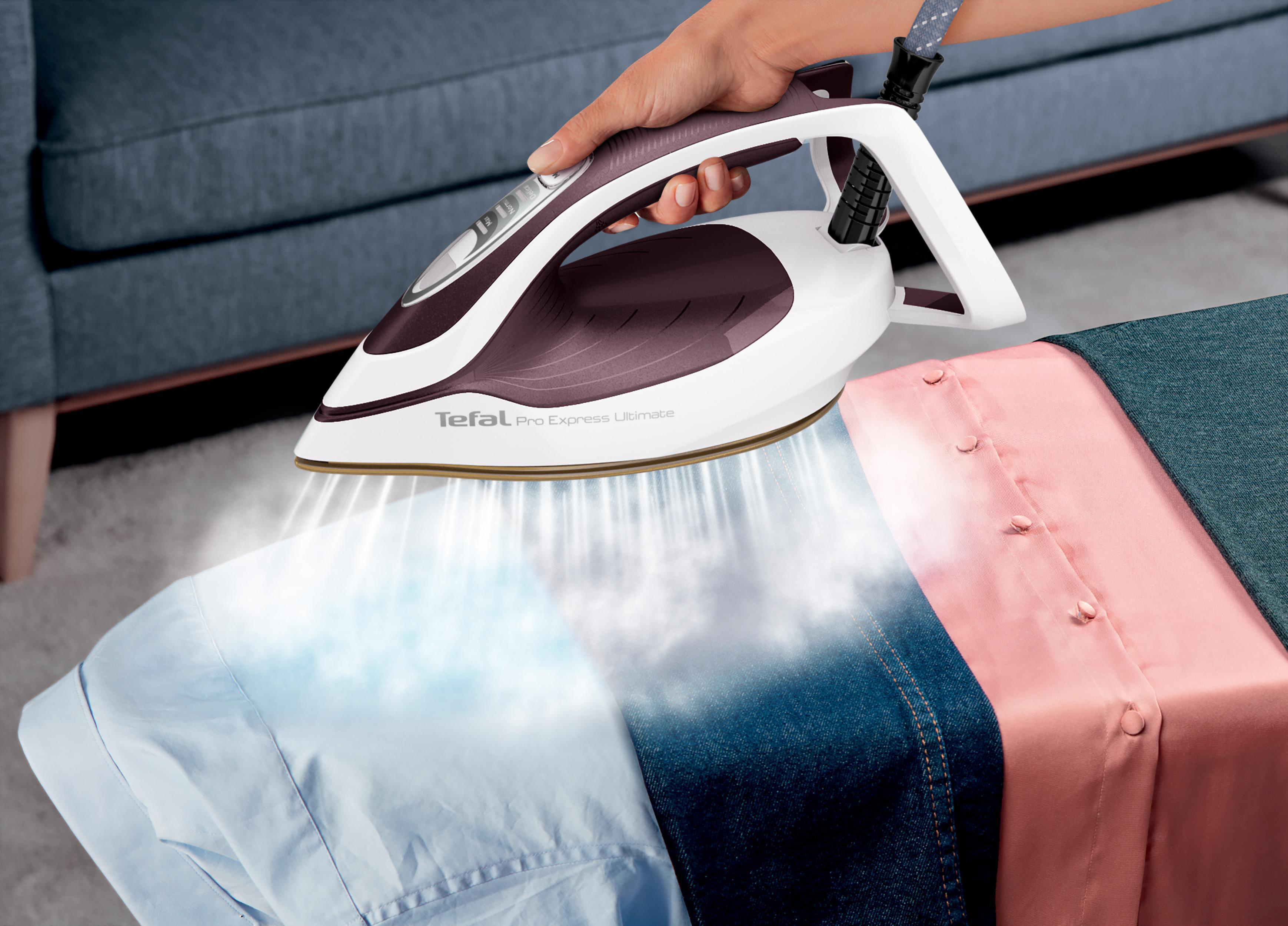 Eine Person bügelt Kleidung mit einem Tefal-Bügeleisen. Dampf ist sichtbar. Blaue, Jeans- und rosa Hemden werden gebügelt.