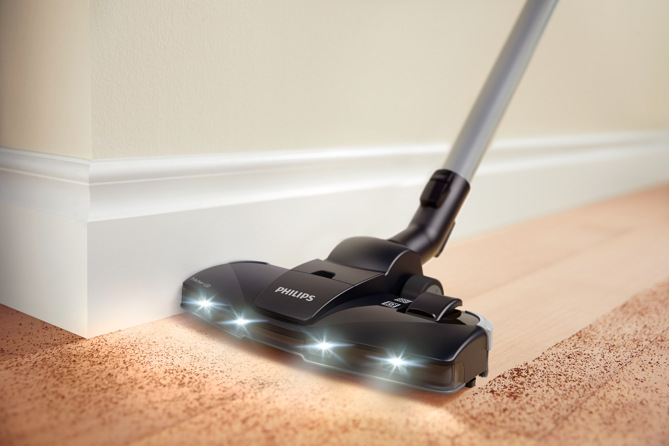 Een Philips stofzuigerkop met lampen aan, die een houten vloer bij een muur schoonmaakt.