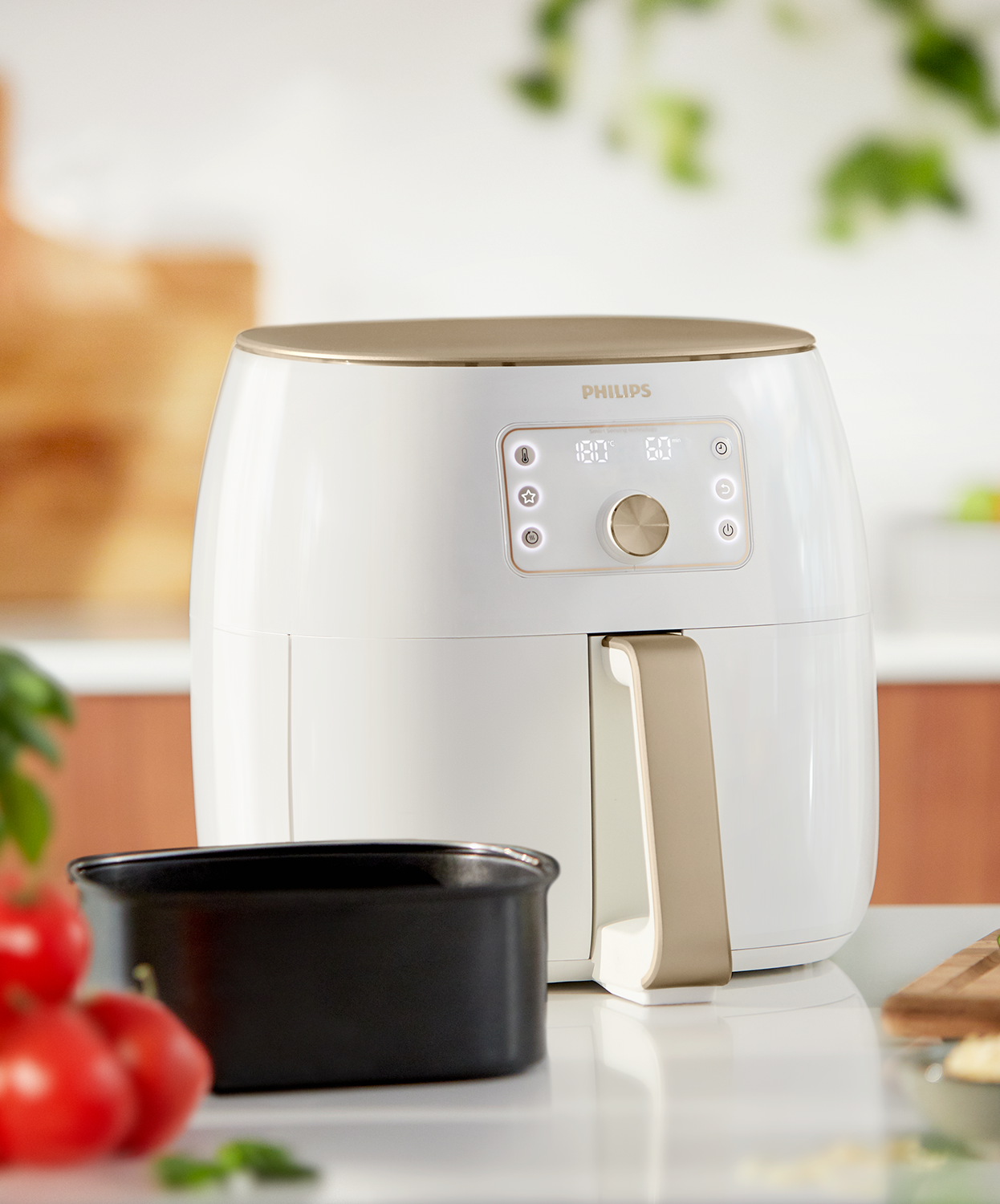 White air fryer with gold accents, black basket, and tomatoes on a white surface.