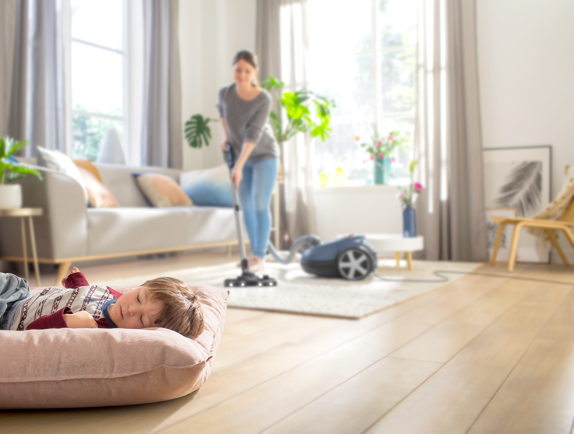 Een vrouw stofzuigt een kamer; een kind slaapt op een roze kussen.