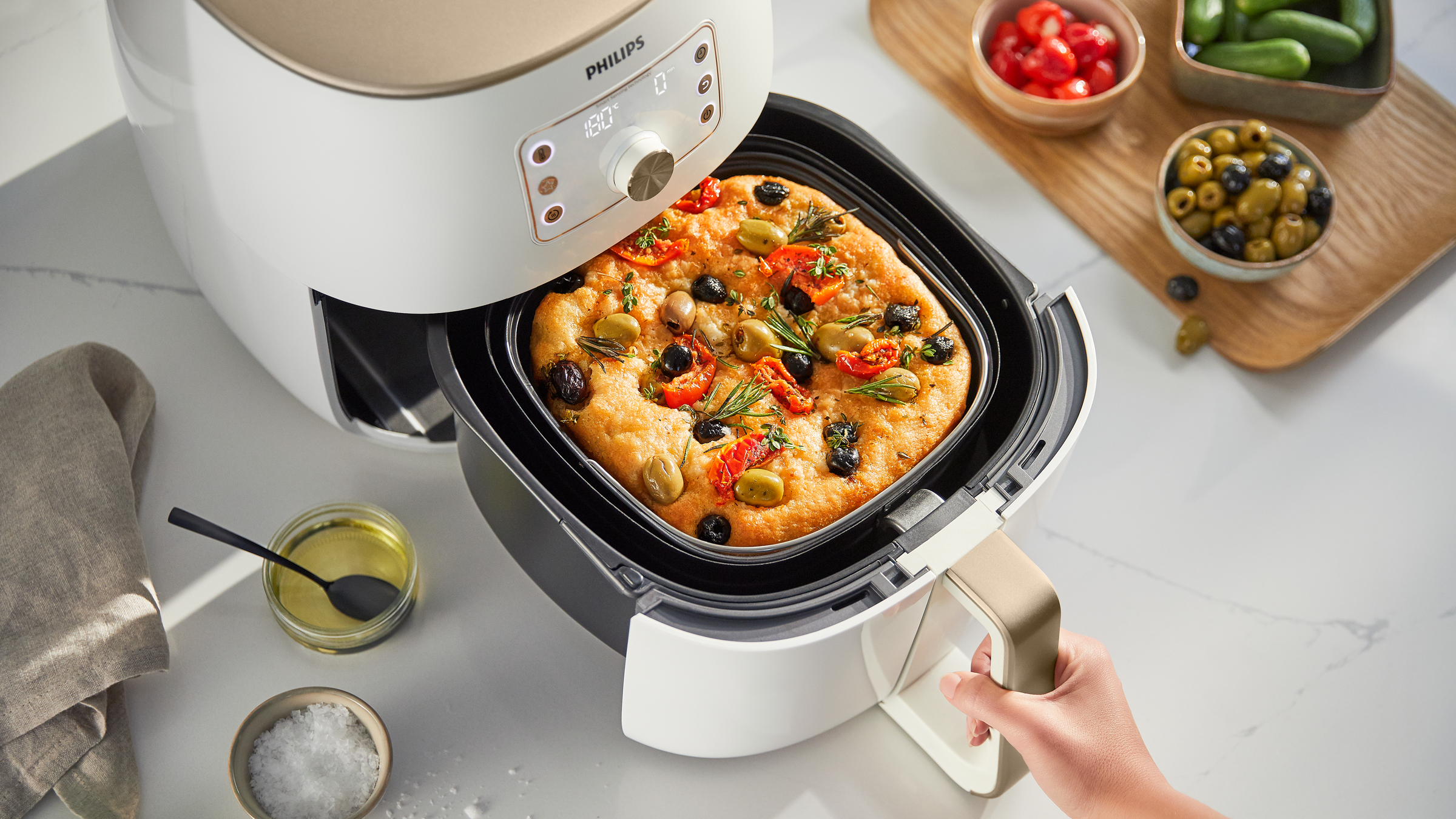 Air fryer with a focaccia and vegetables inside, next to ingredients.