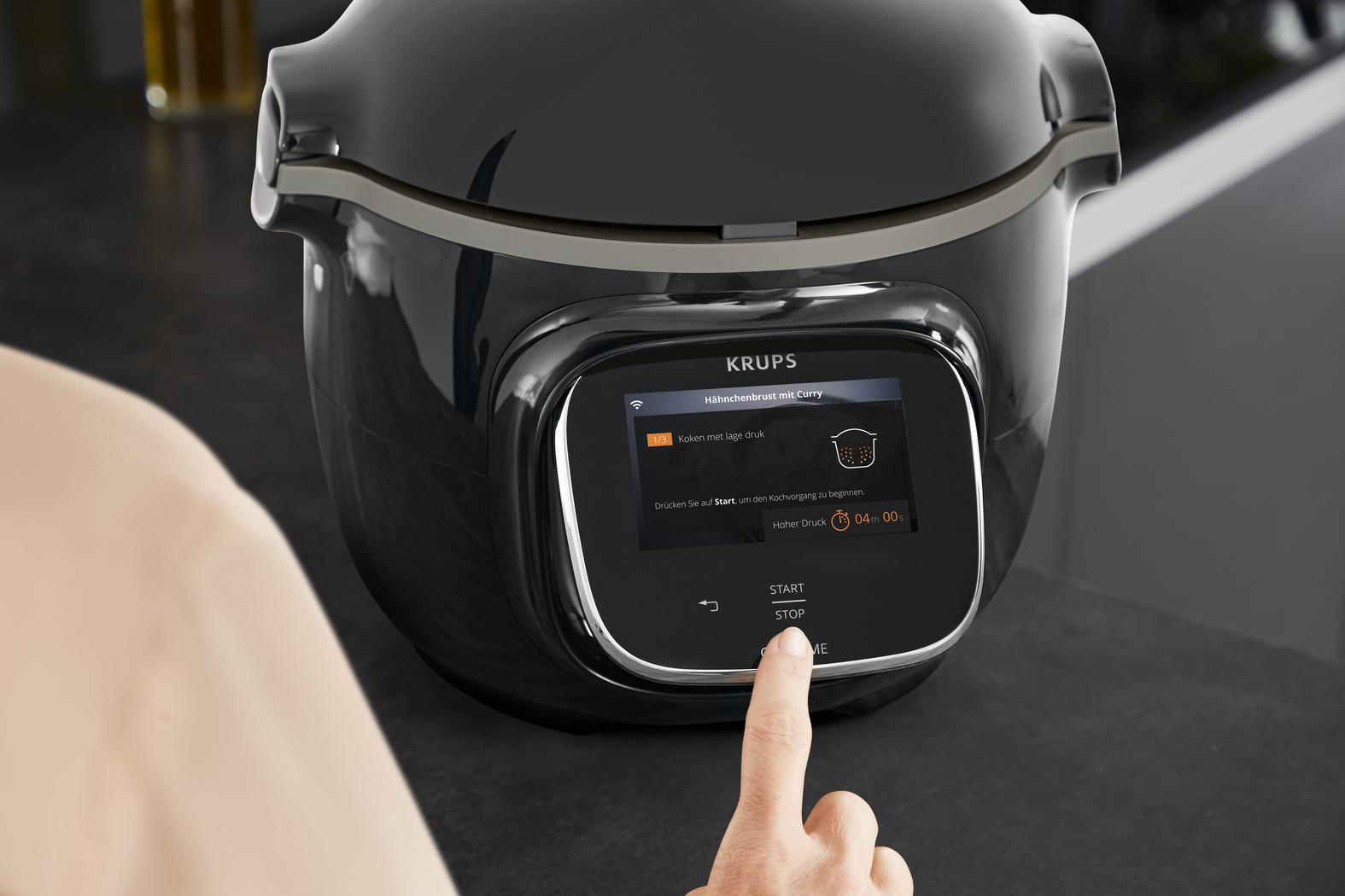 Schwarzer Krups Multikocher mit Touchscreen. Ein Finger drückt die Stopp-Taste.