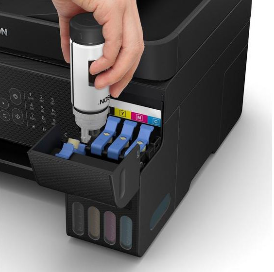 A hand pouring ink into a printer's ink tank. The printer is black, with color ink slots.