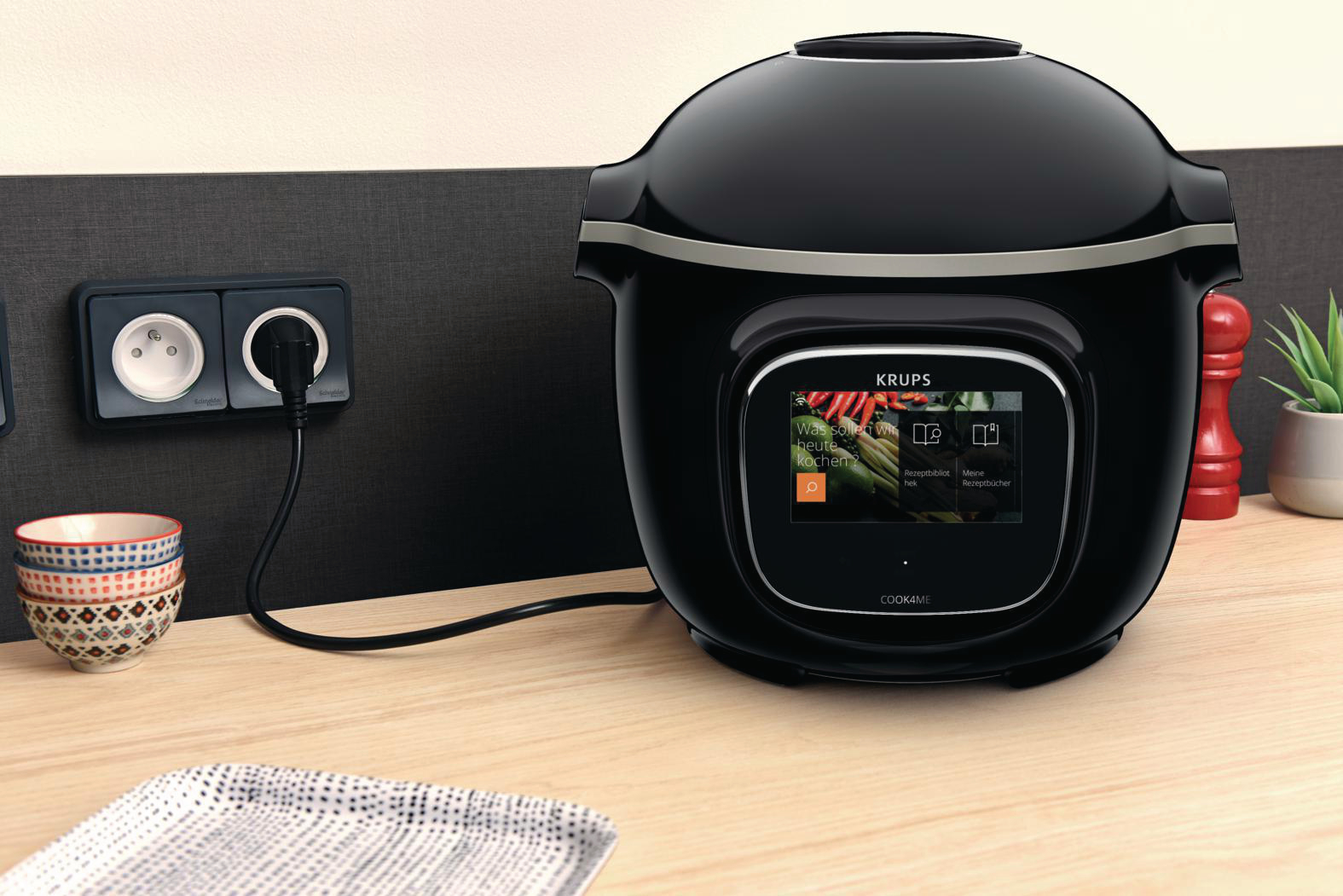 Schwarze Krups Cook4Me+ auf Holzoberfläche, mit Steckdose und Stecker.