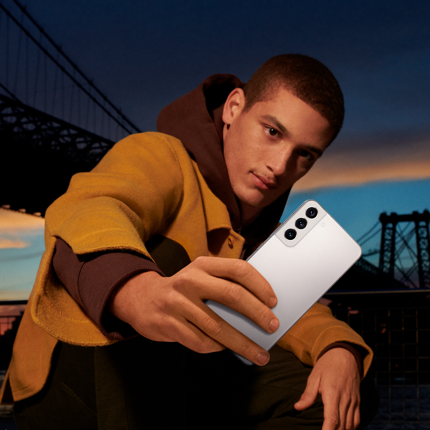 Un hombre sosteniendo un smartphone blanco con un puente de la ciudad al fondo.