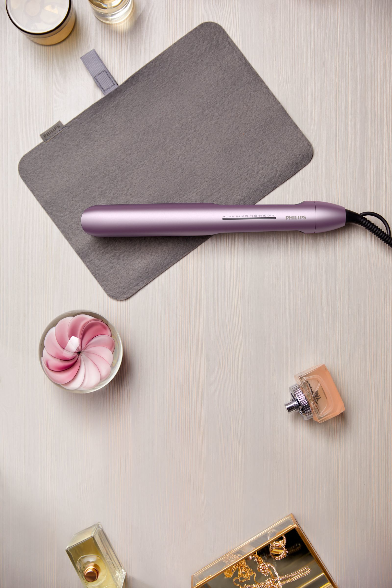 Hair straightener, perfume, and beauty items on a wooden table.