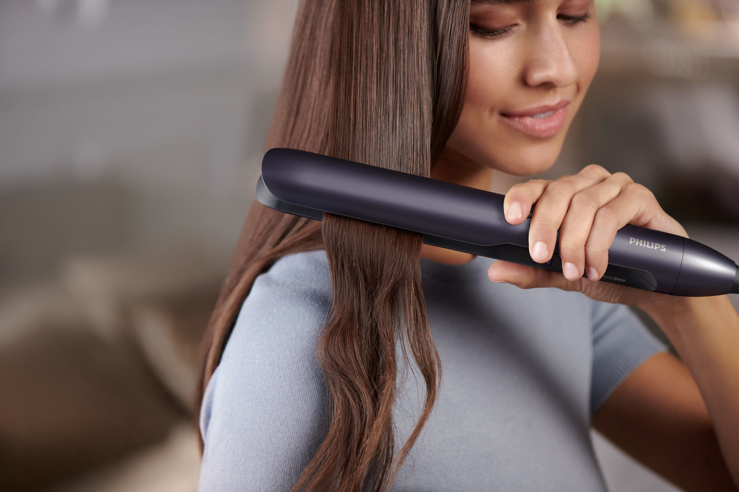A woman uses a Philips hair straightener on her brown hair to straighten it.