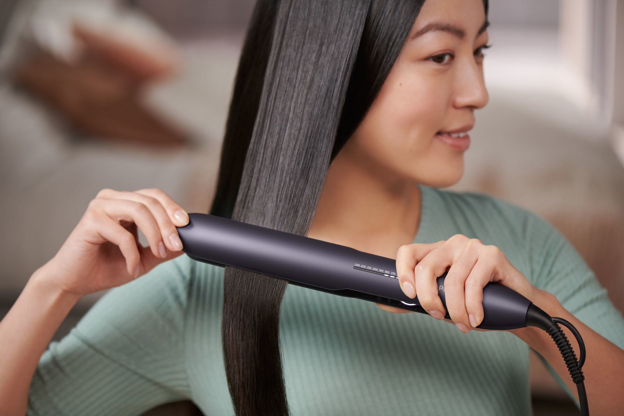 Woman using a hair straightener, hair is straight.