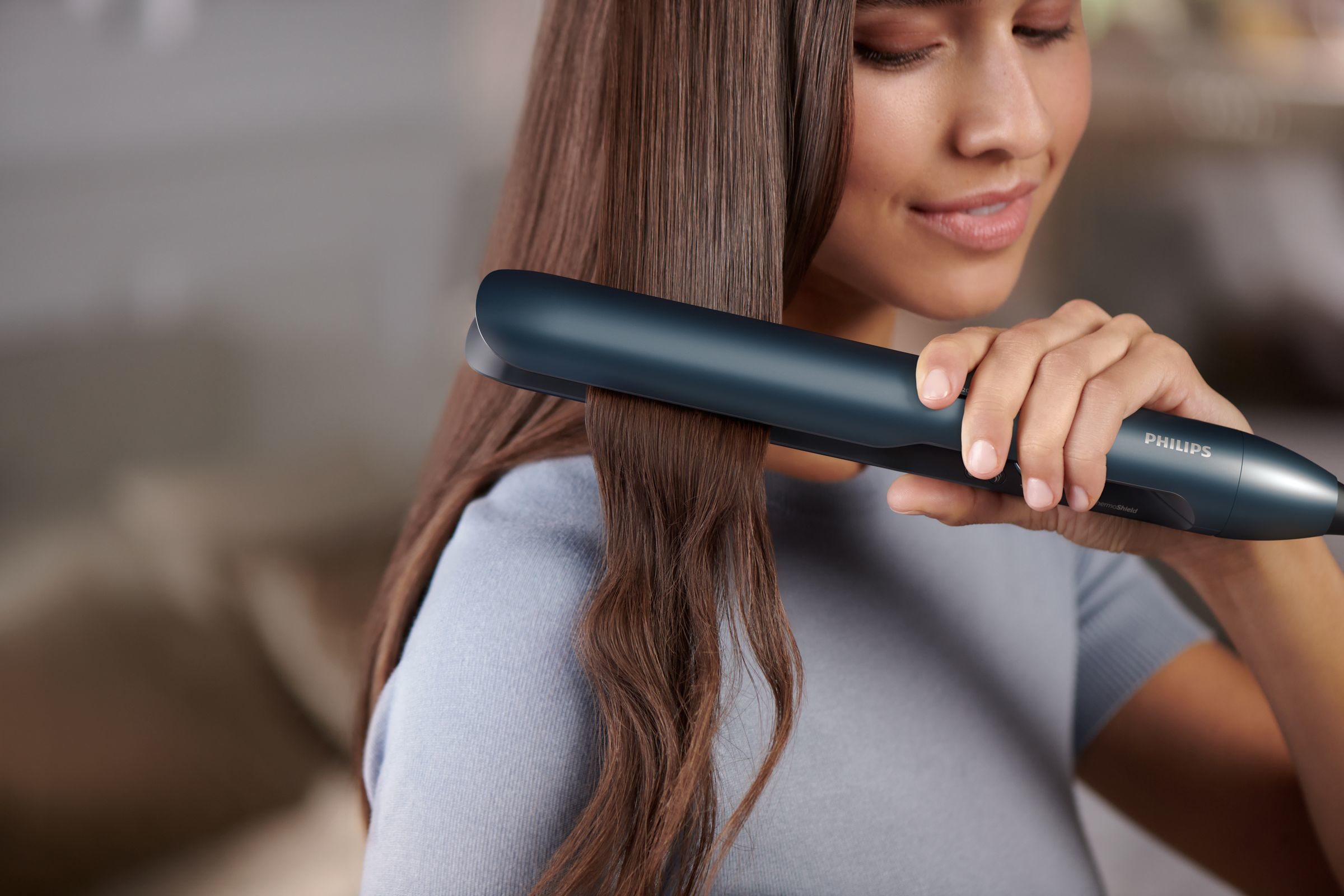 A woman using a blue Philips hair straightener on long, brown hair.