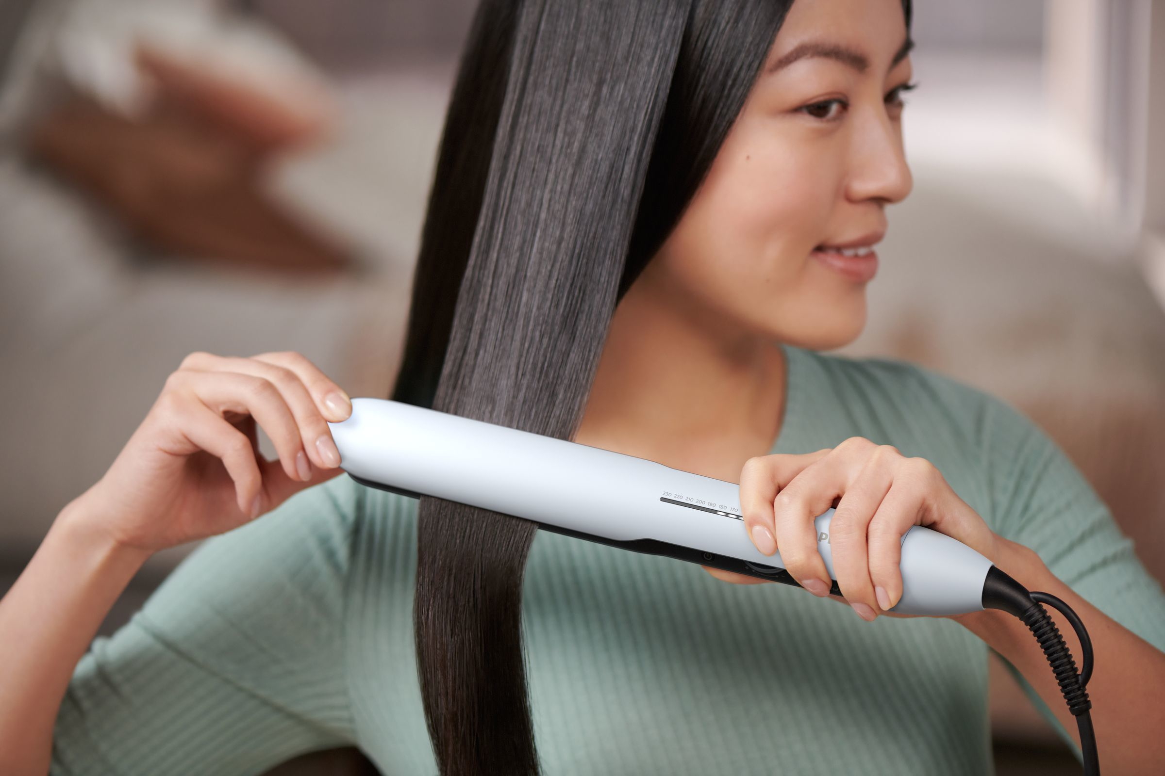 Woman styling her hair with a flat iron. She is smiling and the hair is straight.