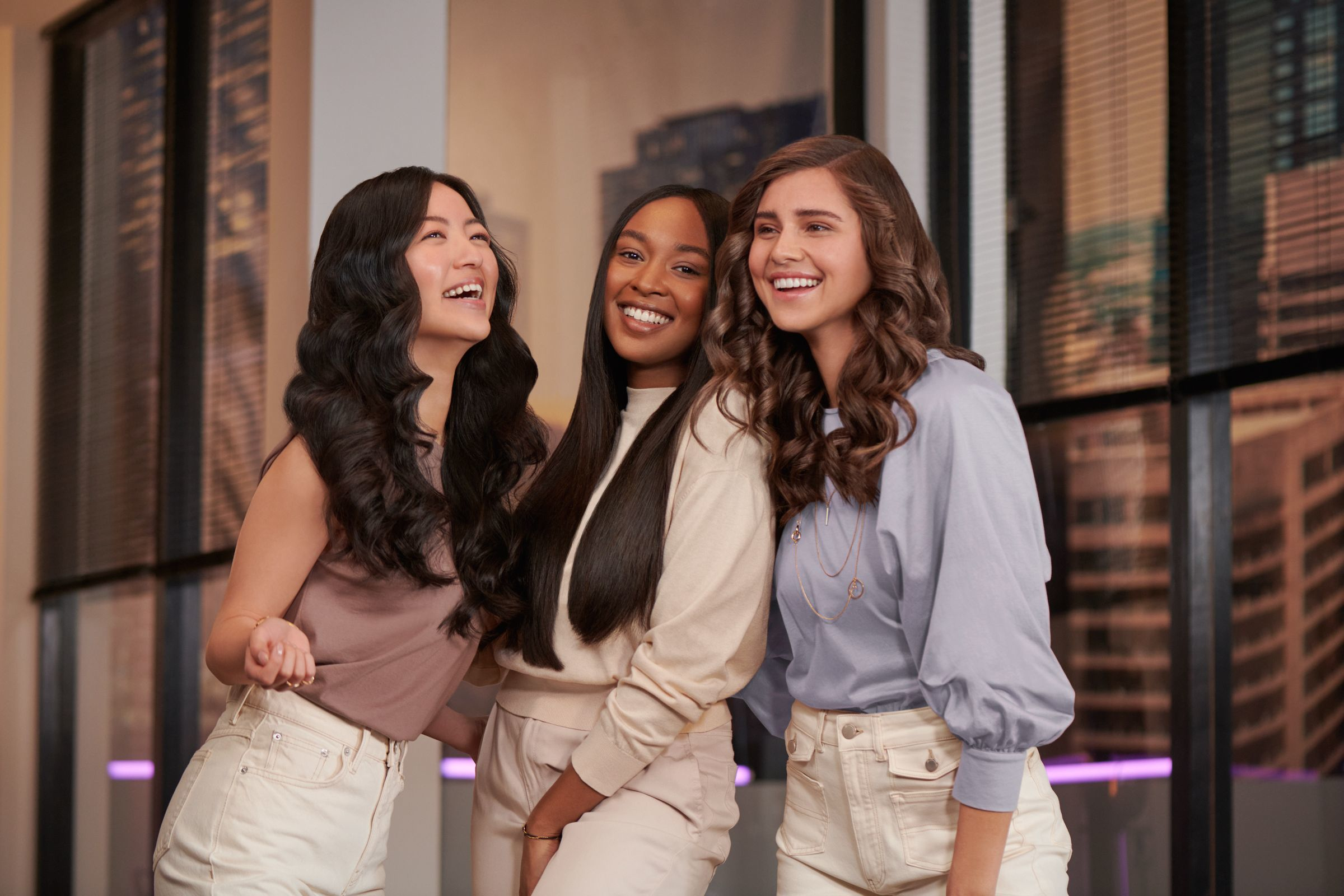 Three diverse women smiling and laughing together. They're in a well-lit setting with a modern design.