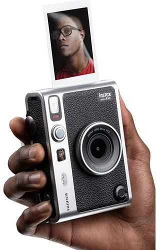 A person holding a silver and black camera with a picture coming out. White background.