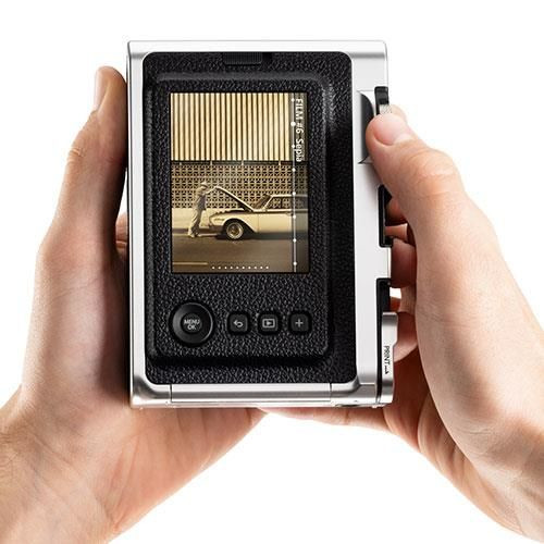 A person holding a silver and black instant camera, showing a photo of a car.