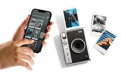 Hands holding a phone displaying photos, next to a camera and prints.