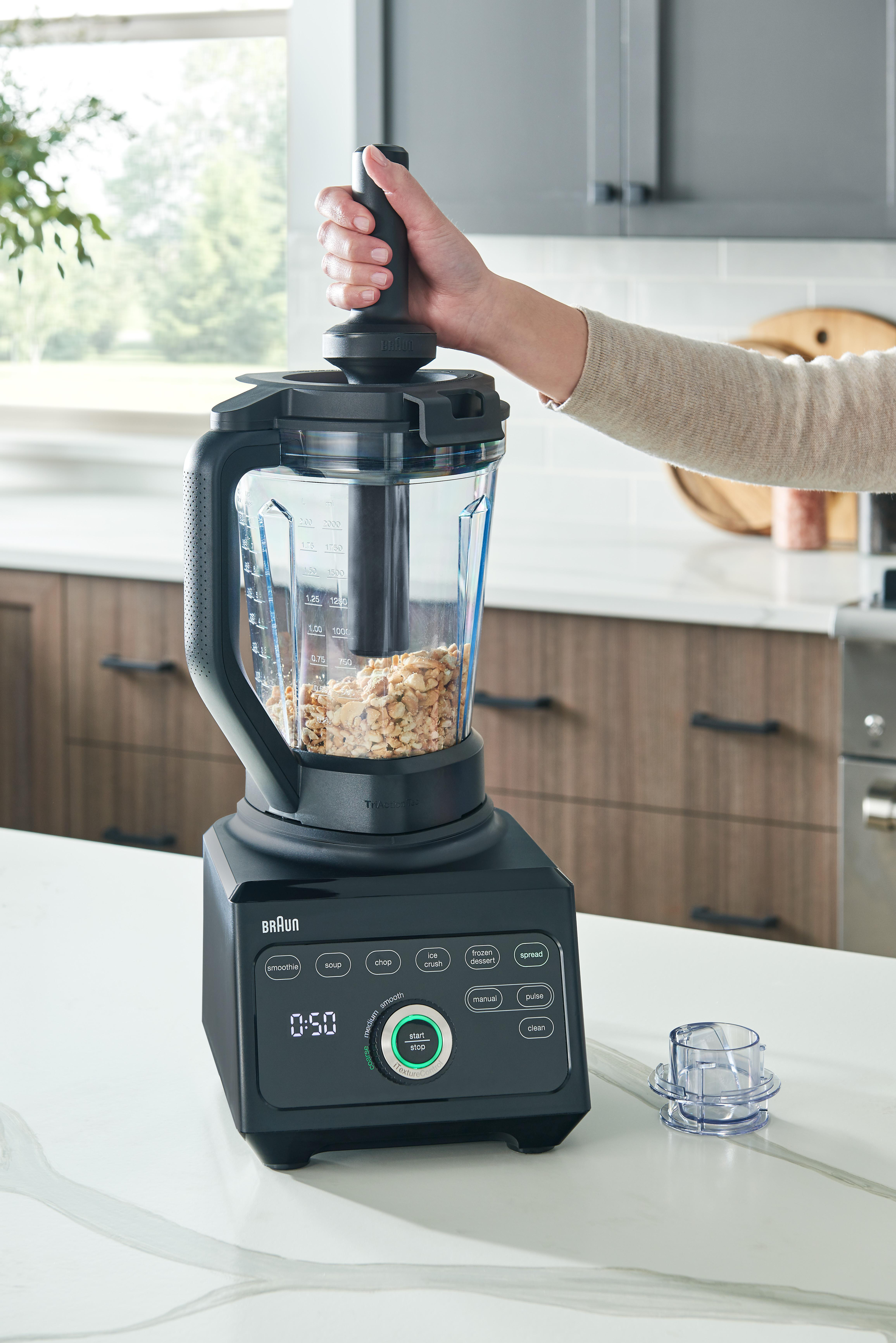 Eine Person, die einen Mixer zum Zerkleinern von Nüssen verwendet. Der Mixer ist schwarz.