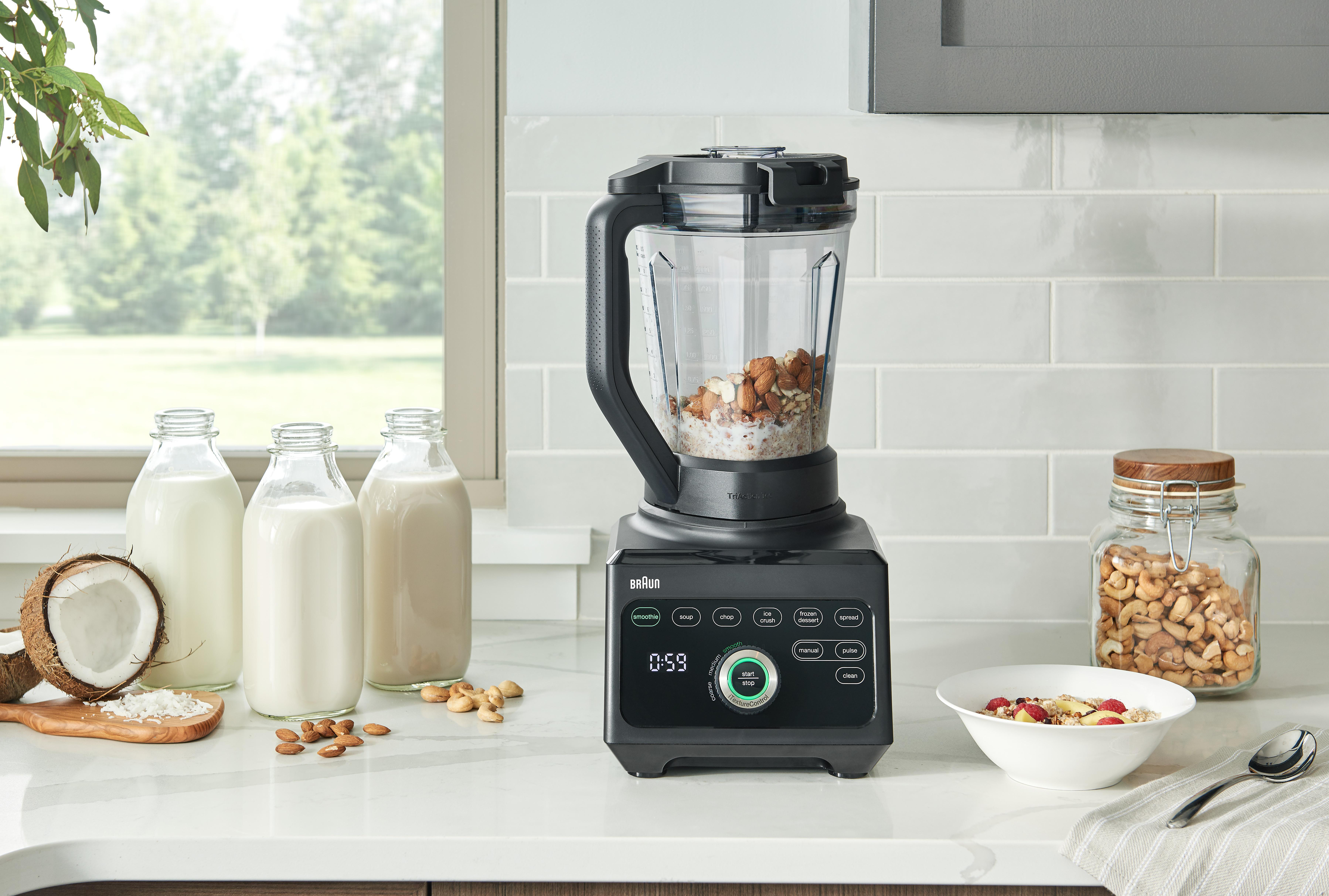 Ein schwarzer Mixer mixt Hafer und Nüsse. Milchflaschen links. Eine Schüssel mit Essen rechts.