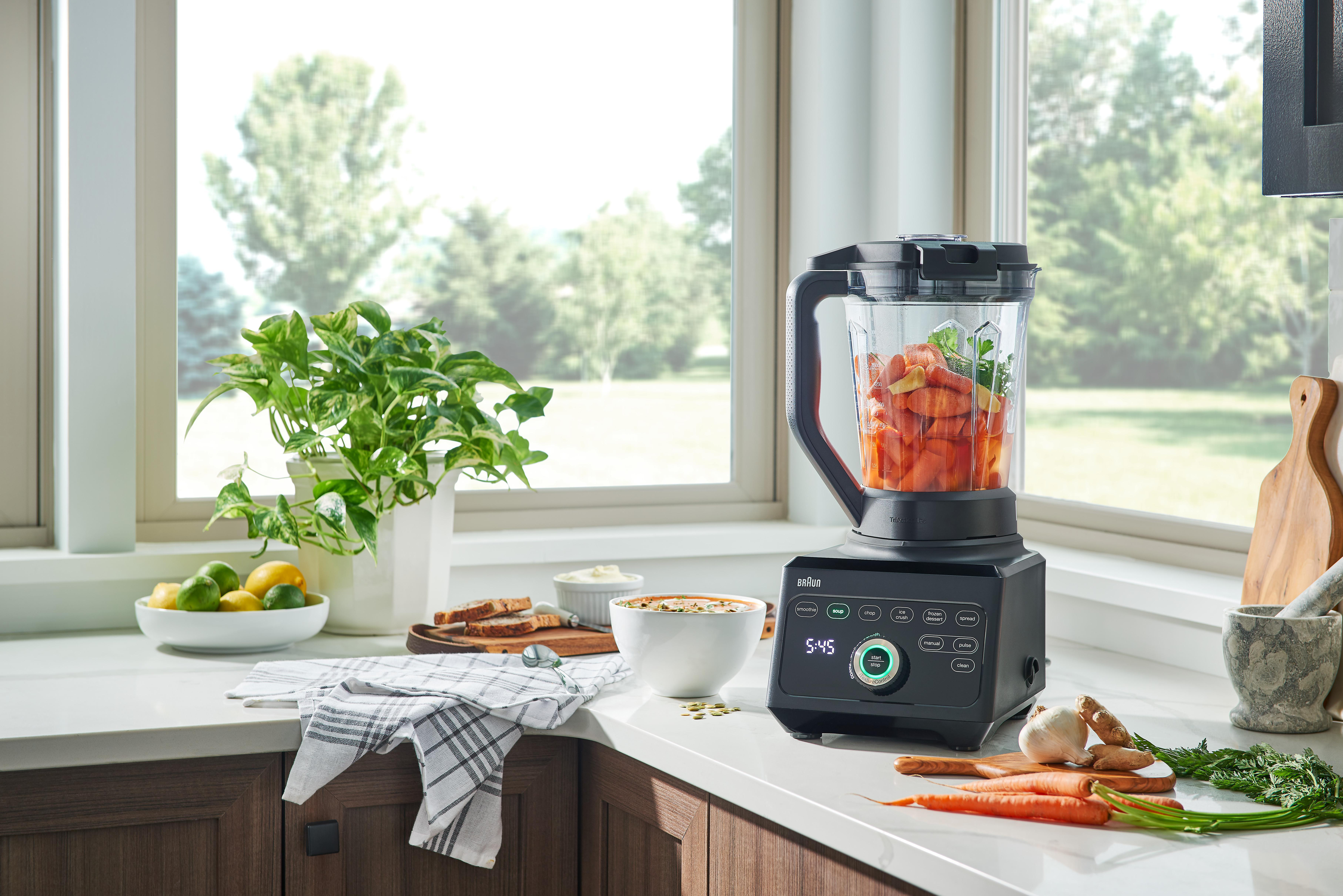Ein Mixer auf einer Theke mit Essen darin, umgeben von Zutaten und Küchenutensilien.