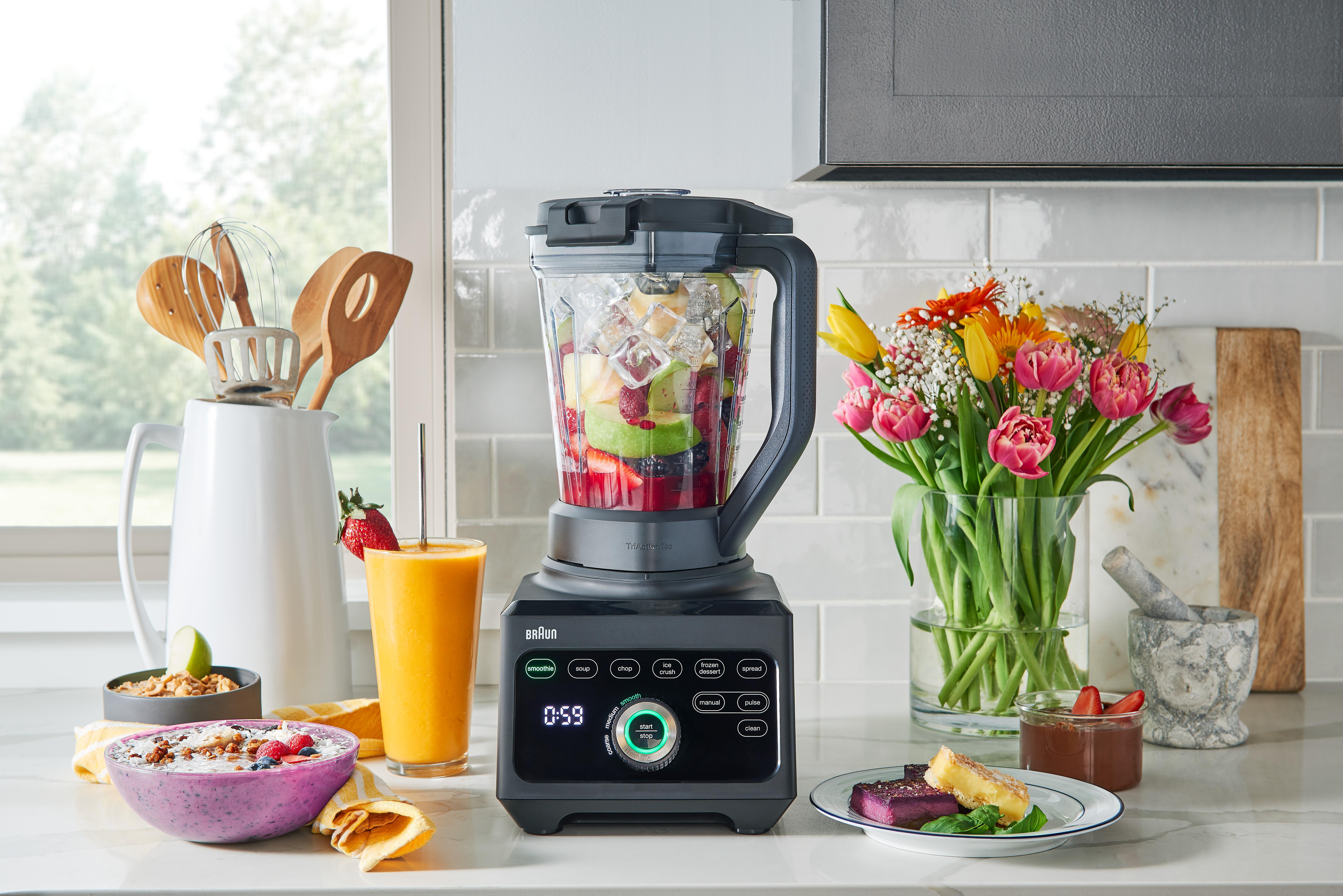 Mixer mit Früchten und Gemüse, Smoothie, Blumen und eine kleine Schüssel mit Zutaten.