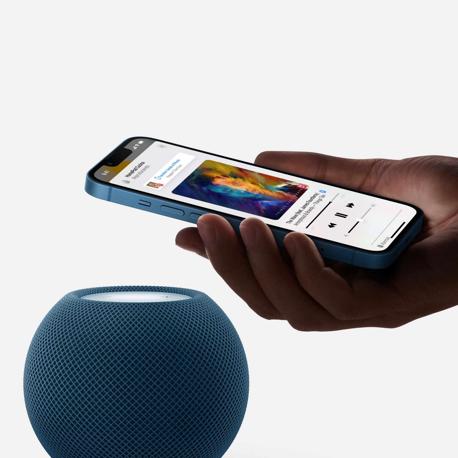 Una persona sosteniendo un teléfono azul con música reproduciéndose junto a un HomePod mini azul.