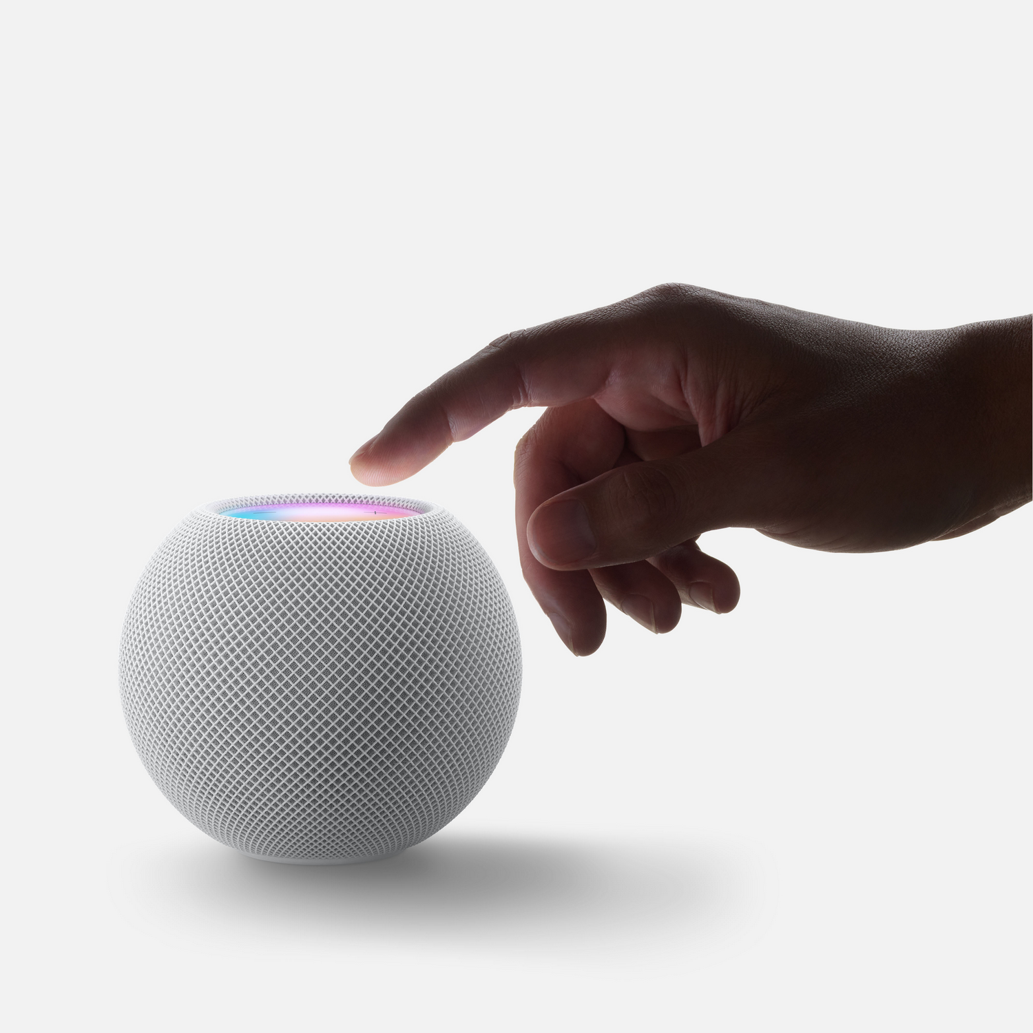 Una mano toca un altavoz inteligente blanco. La parte superior emite luz de colores.