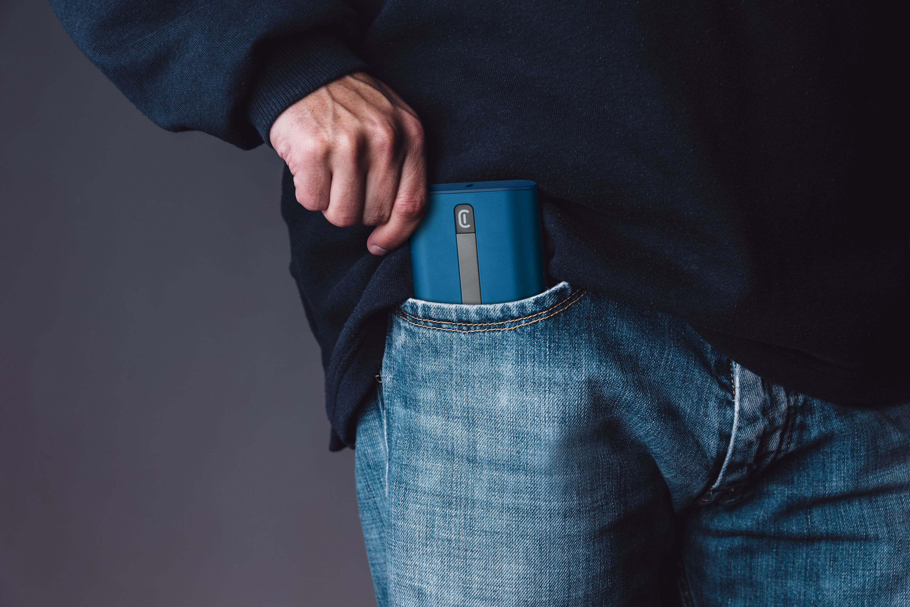Une main mettant un appareil rectangulaire bleu à bande grise dans une poche de jean.