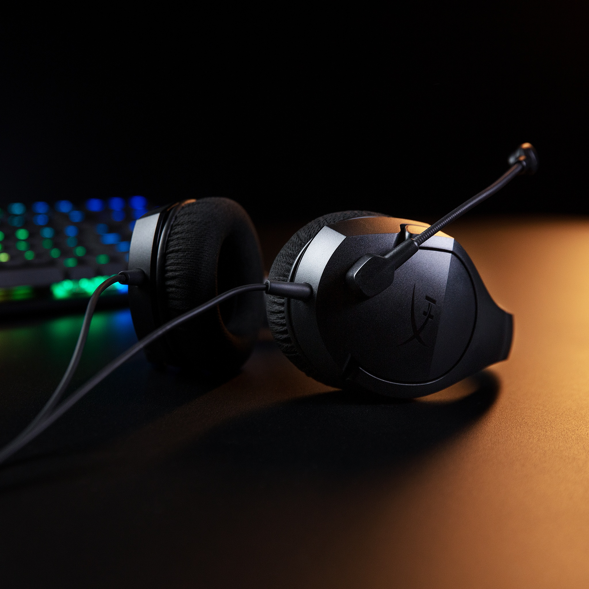 Fekete gamer fejhallgató mikrofonnal. A háttérben egy billentyűzet látható. Sötét felület.