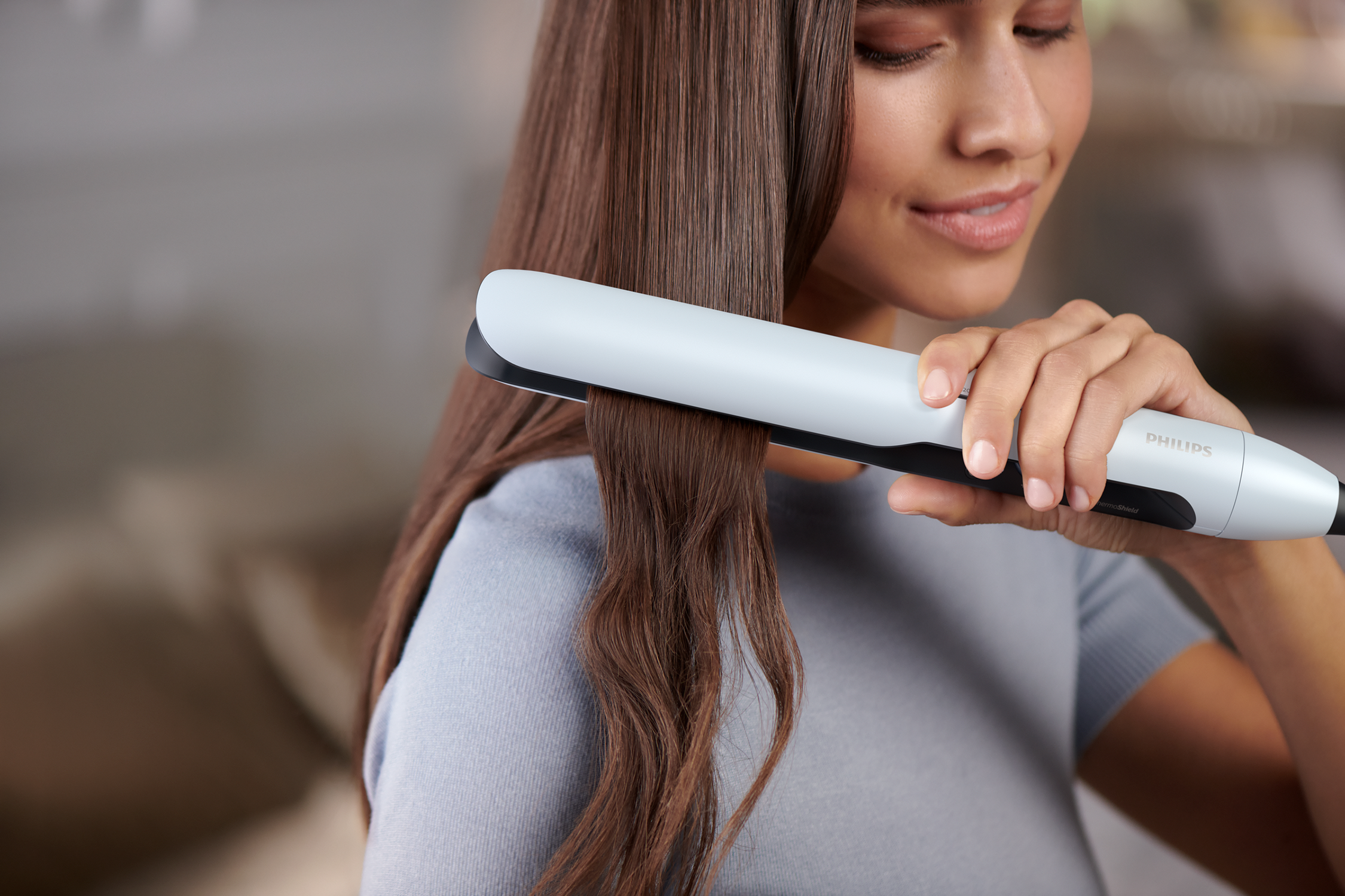 A woman straightening her hair with a gray and black hair straightener.