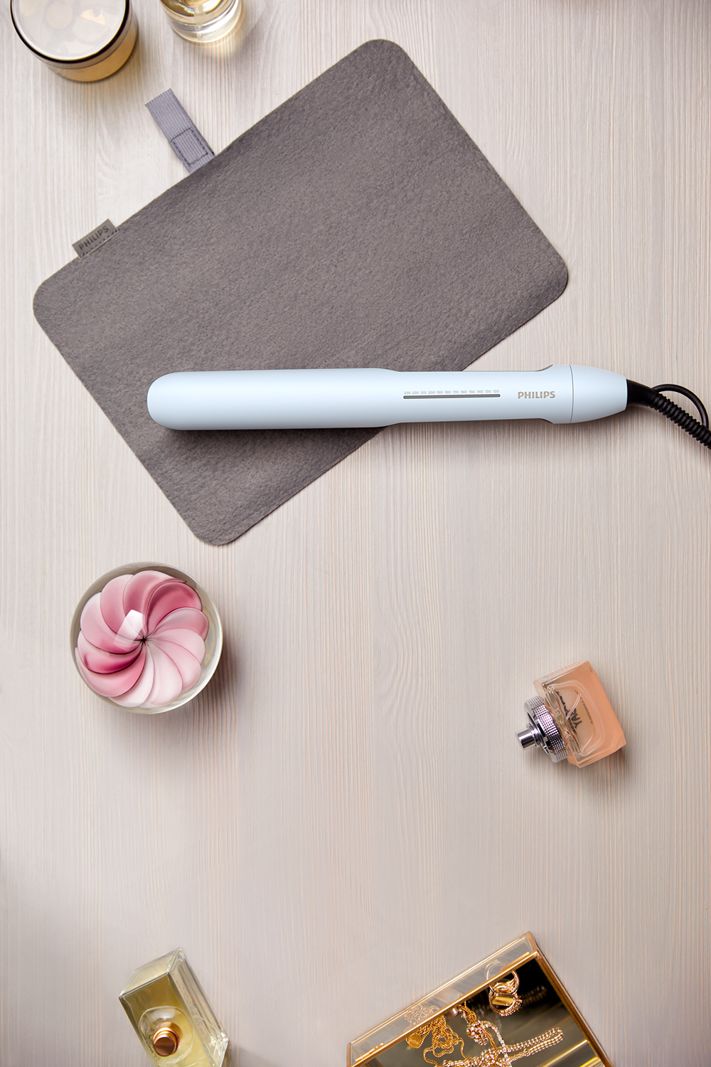 Top view of a light blue hair styler, with a gray case, perfume bottles, and accessories on wood.
